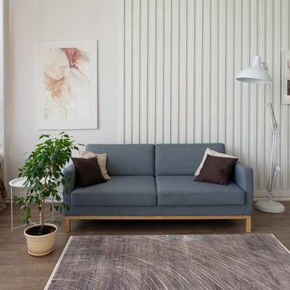 Modern living room with dark grey sofa, white accents, big plant, featuring a modern rug with distressed design on grey and earthy tones