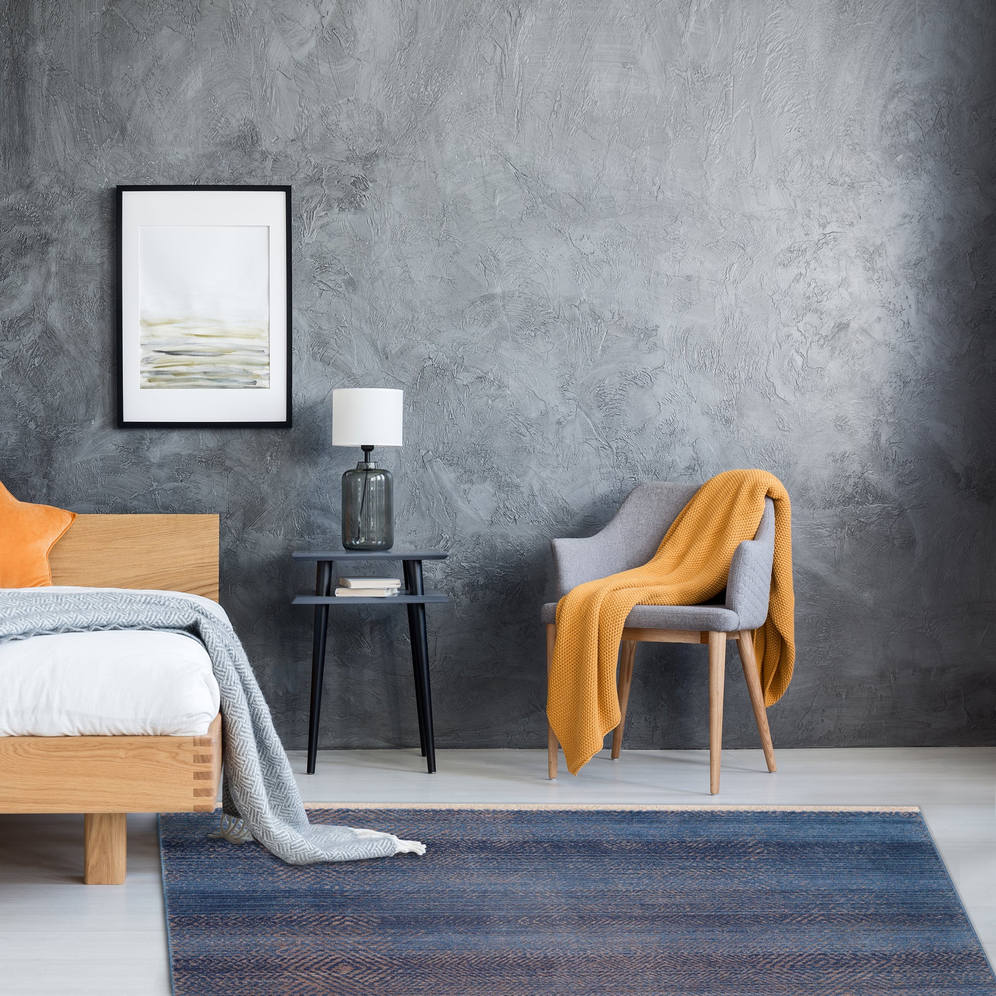 Grey minimalist bedroom with Mystic Navy Rug, grey armchair, yellow throw